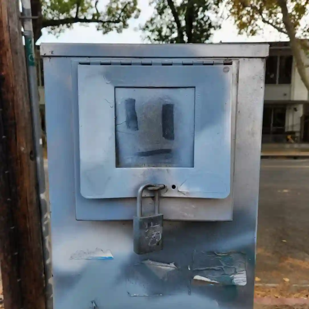 A close-up of a worn and battered public utility box, with a simple hand-drawn face that appears anxious. The effect is of a robot, uncertain of its purpose.